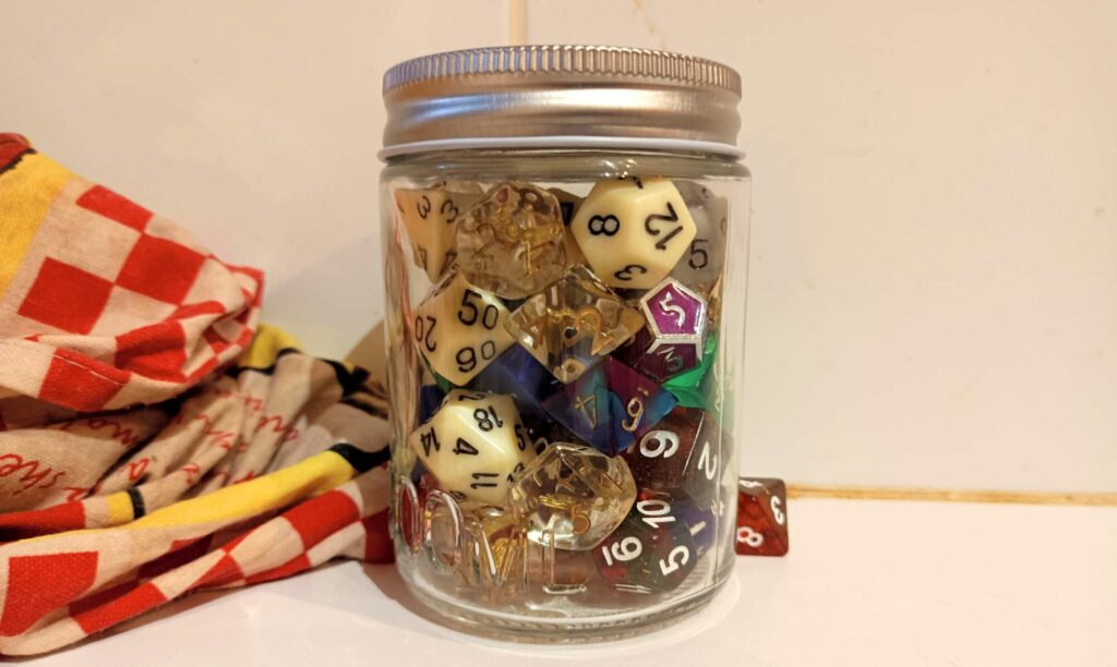 a jam jar full of gaming dice, with a spilled die and a teatowel beside it